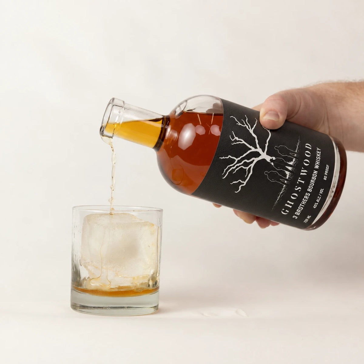 Pouring Ghostwood 3 Brothers Bourbon over a large ice cube