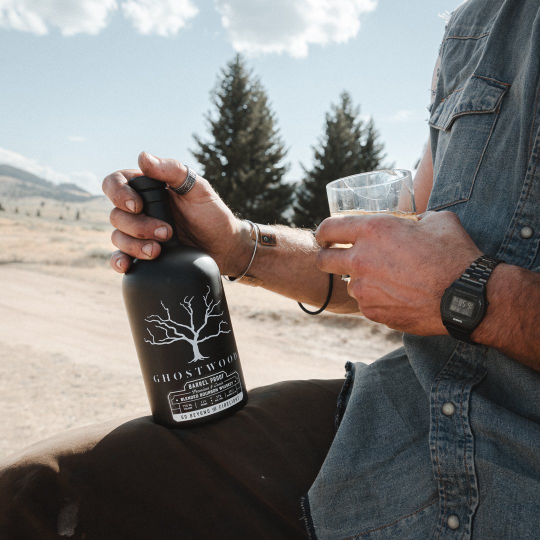 Ghostwood Barrel Proof Black with a pour, pine trees and big sky behind