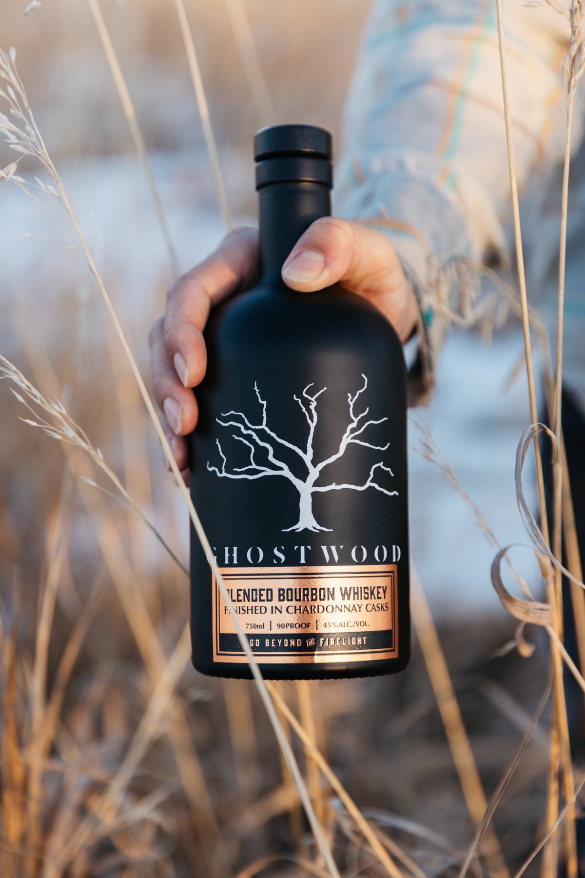 Ghostwood Chardonnay Cask bottle held in tall autumn grass